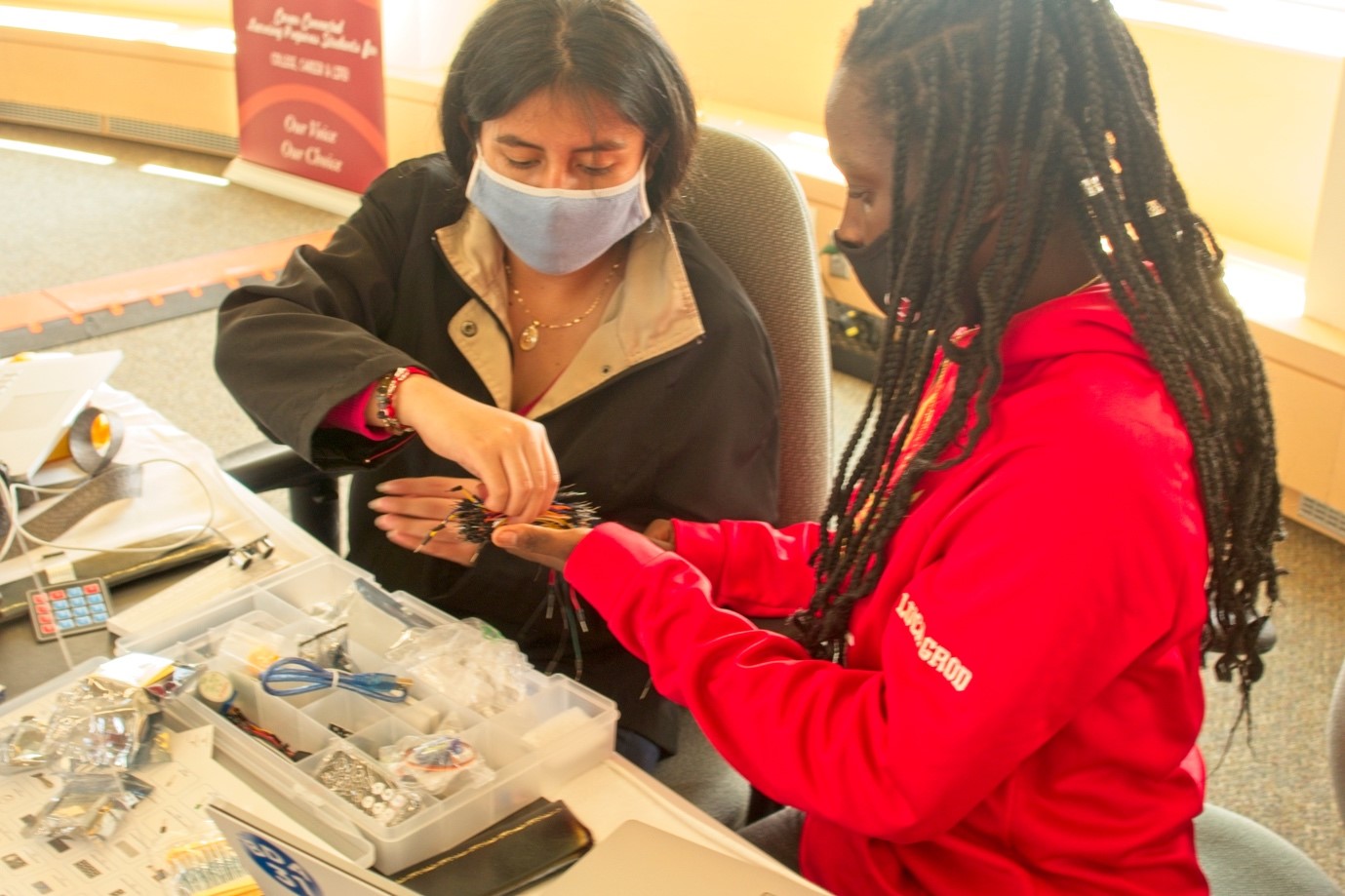 A person wearing a mask and sitting next to a person wearing a mask

Description automatically generated