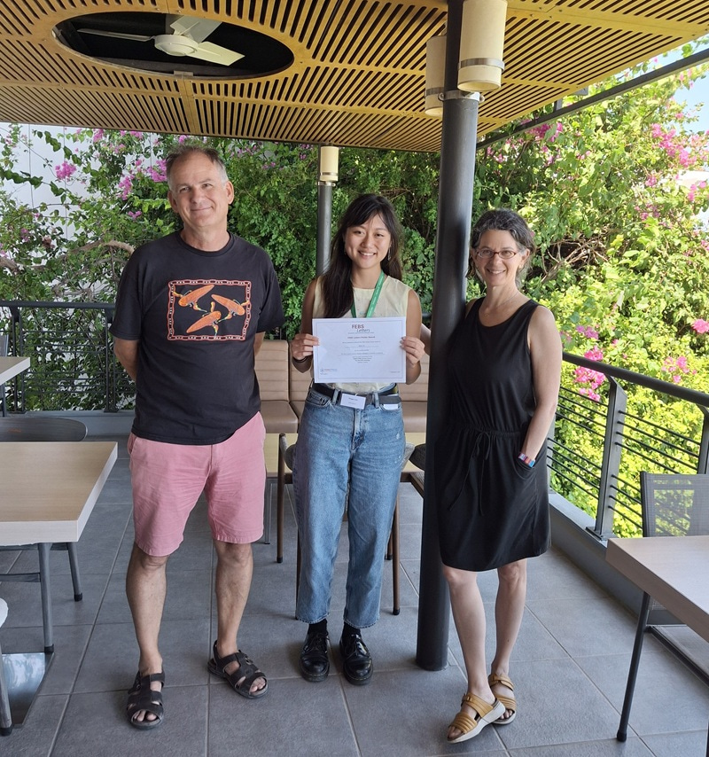 Three people standing facing the camera, with the middle young woman holding a certificate.