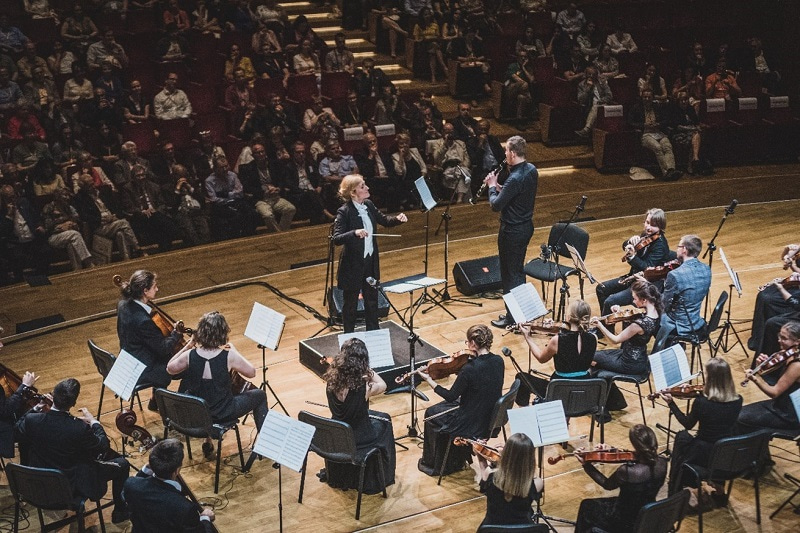 Photo of a classical music orchestra performing in a hall, watched by Congress attendees.