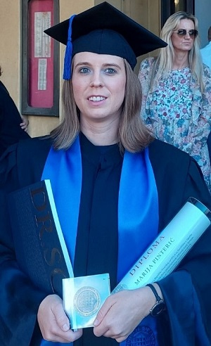 Photo of Marija Pinterić wearing her graduation gown and holding her diploma certificate.