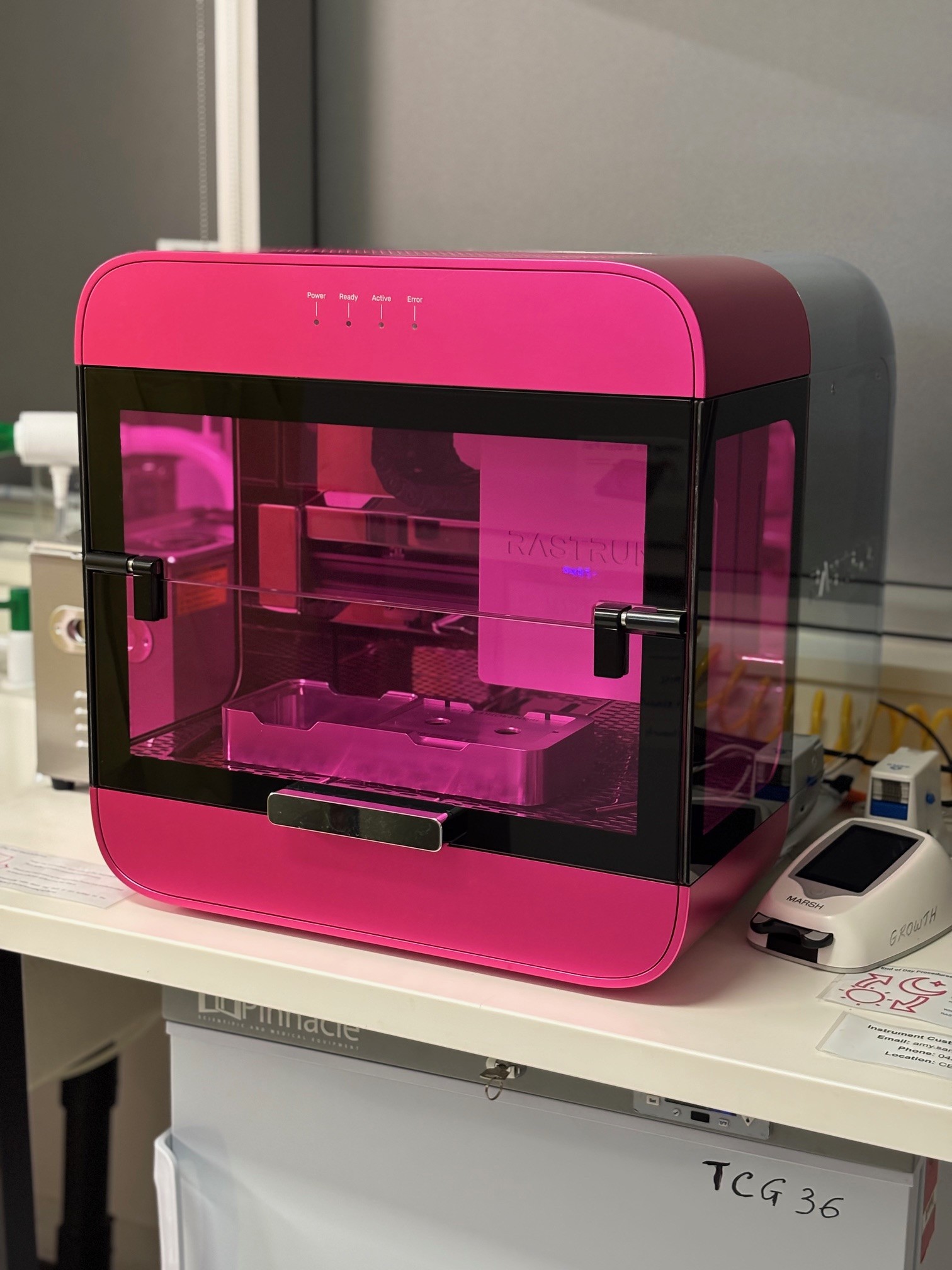 Pink bioprinter on white lab bench.