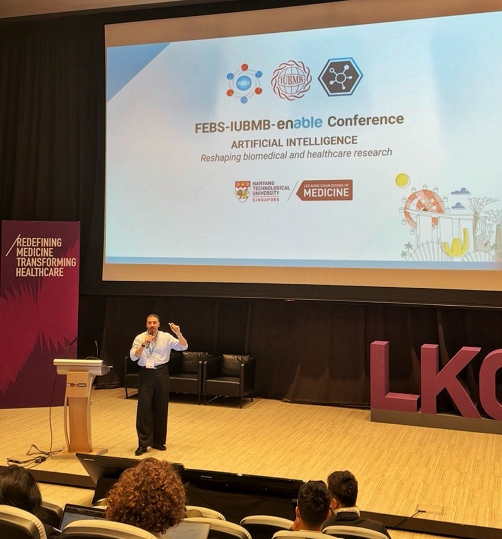 Photo taken from the audience of the author presenting on a stage, with the screen behind him.