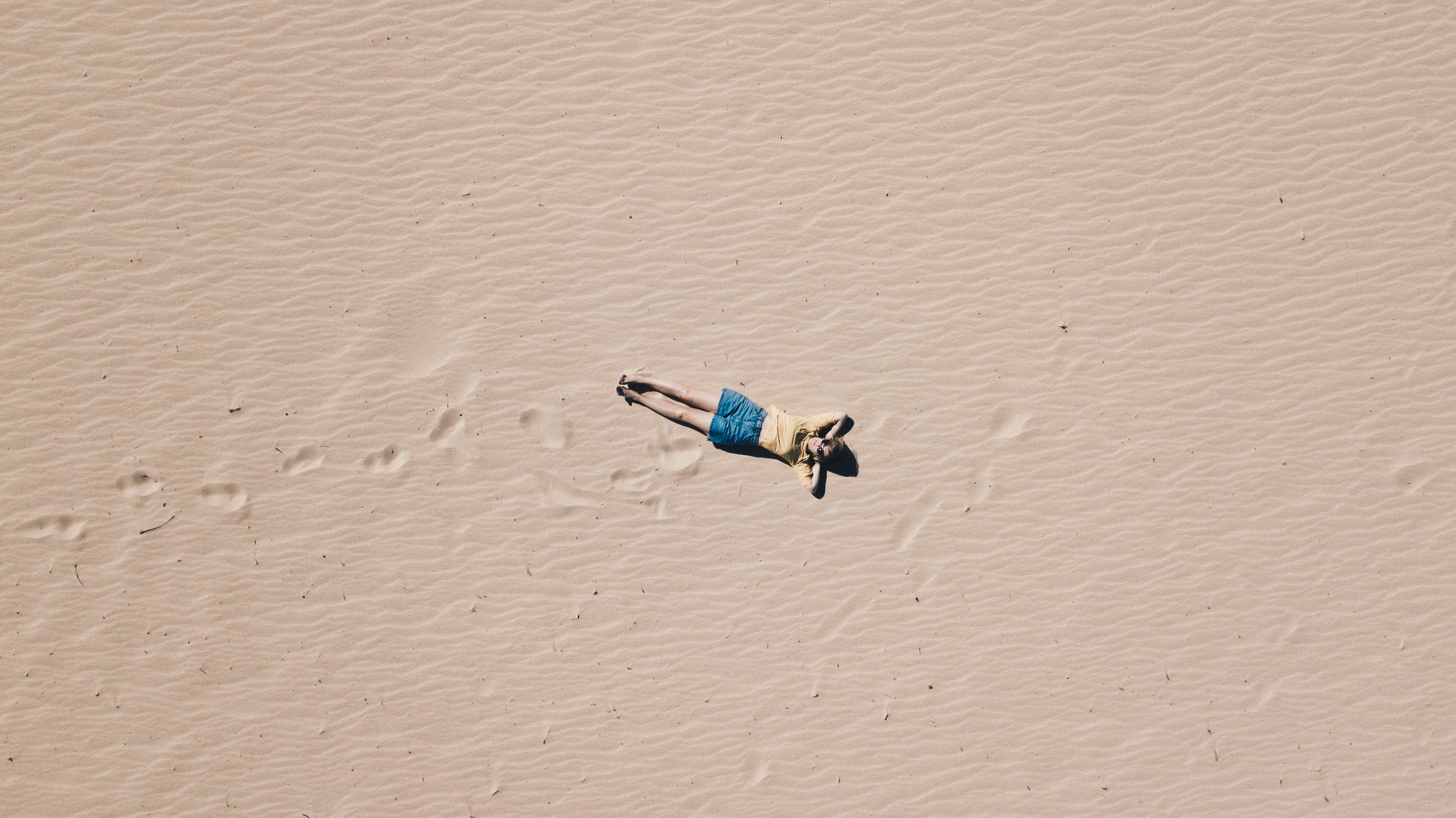 A woman lying on the sand. She is giving off a relaxed vibe. Photo by Emilio Garcia on Unsplash.