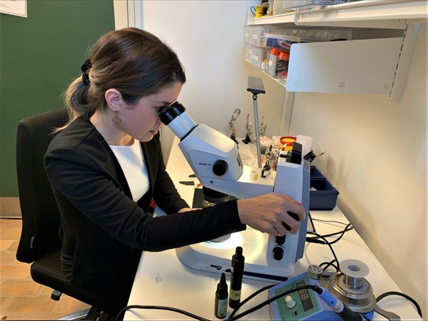 Woman sitting down at a desk and looking into a microscope.