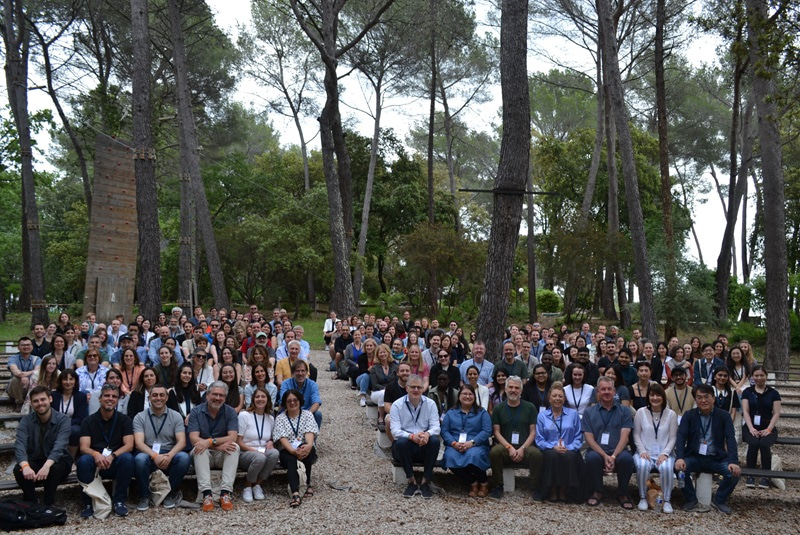 Photo of a large group, sitting with trees behind them.