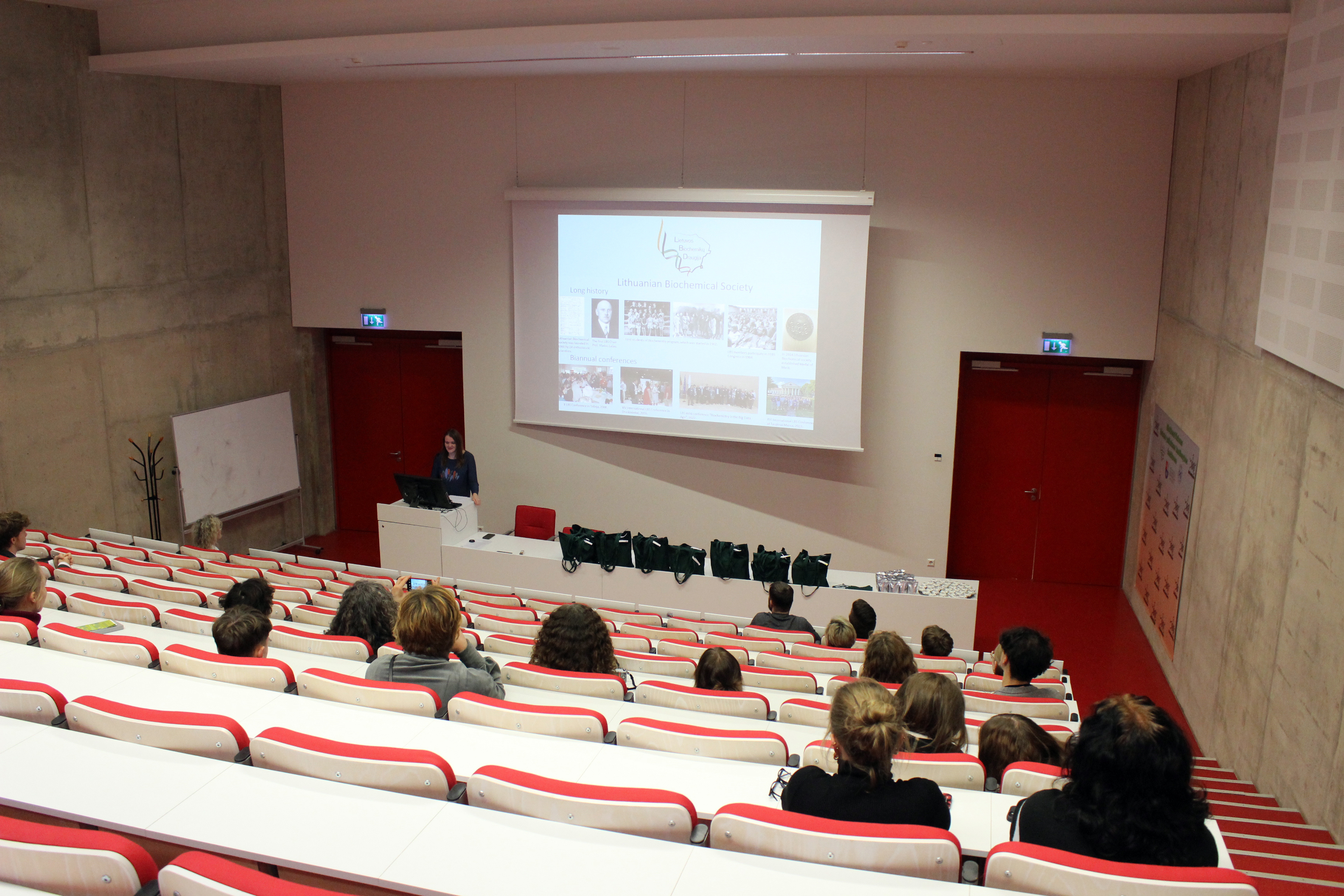 Photo of a lecture hall, taken from a row high up, showing rows further down and the stage.