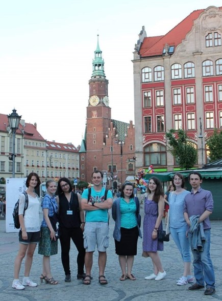 Group photo of eight people facing the camera, standing on a square with a church spire in the background.