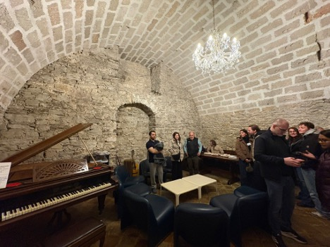 People, a piano and seats in an old cave-like building.