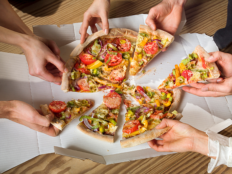 A photo of sliced pizza and many hands grabbing slices. 