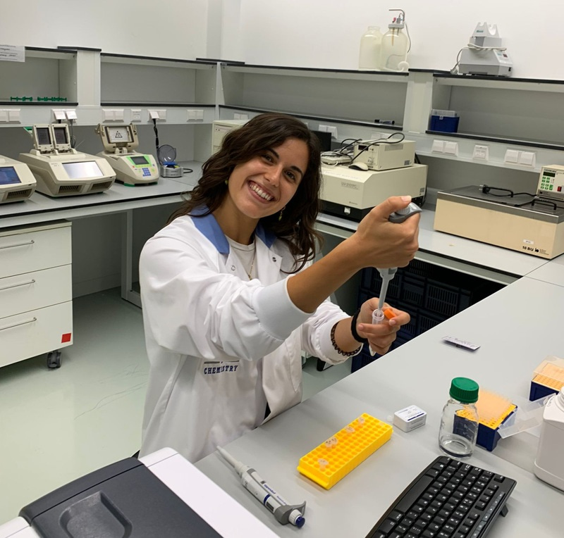 Photo of Cristina  V. Lopez Gallego holding a pipette and a tube, and smiling at the camera.