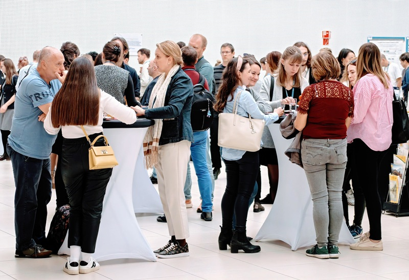 Group photo of people standing around high tables and talking between them.