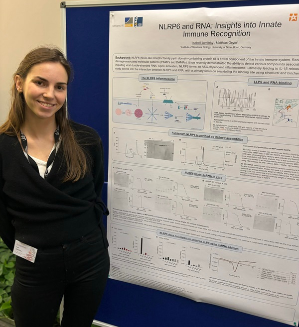Photo of Isabell Jamitzky standing to the left of a poster showing her research.