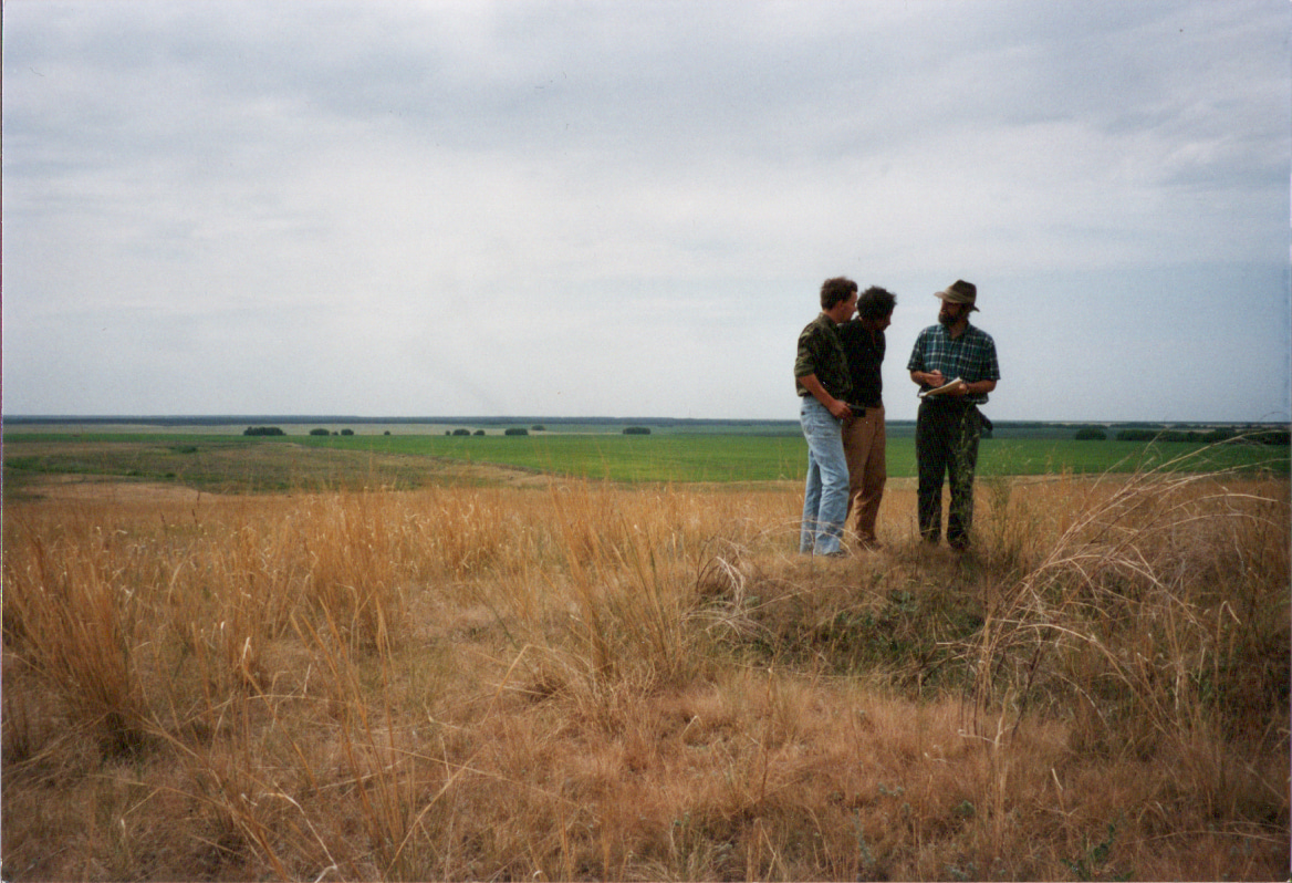 Co-authors David Anthony (right), Pavel Kuznetsov, and Oleg Mochalov stand in 1995 on a kurgan in the treeless steppe overlooking the broad Samara River valley; the green line on the horizon is the Samara floodplain gallery forest, a narrow ribbon of forest and riverine resources running through low-resource steppes. Before the Yamnaya period the steppe was little used or occupied; its biomass became available to humans through high-mobility pastoralism, invented in the late 4th millennium BCE.  