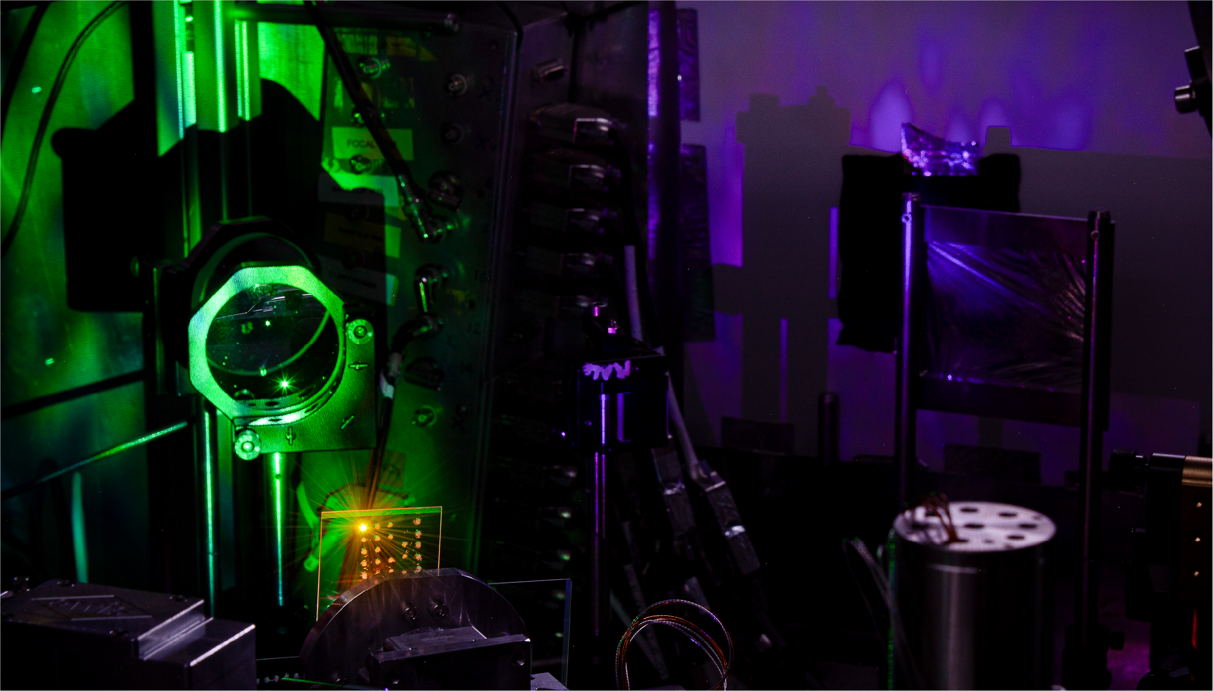 The vacuum chamber during the interaction. A relativistically intense laser pulse is focused on the glass target. The interaction generates a green glowing plasma and a purple harmonic beam that contains extreme coherent light fields.