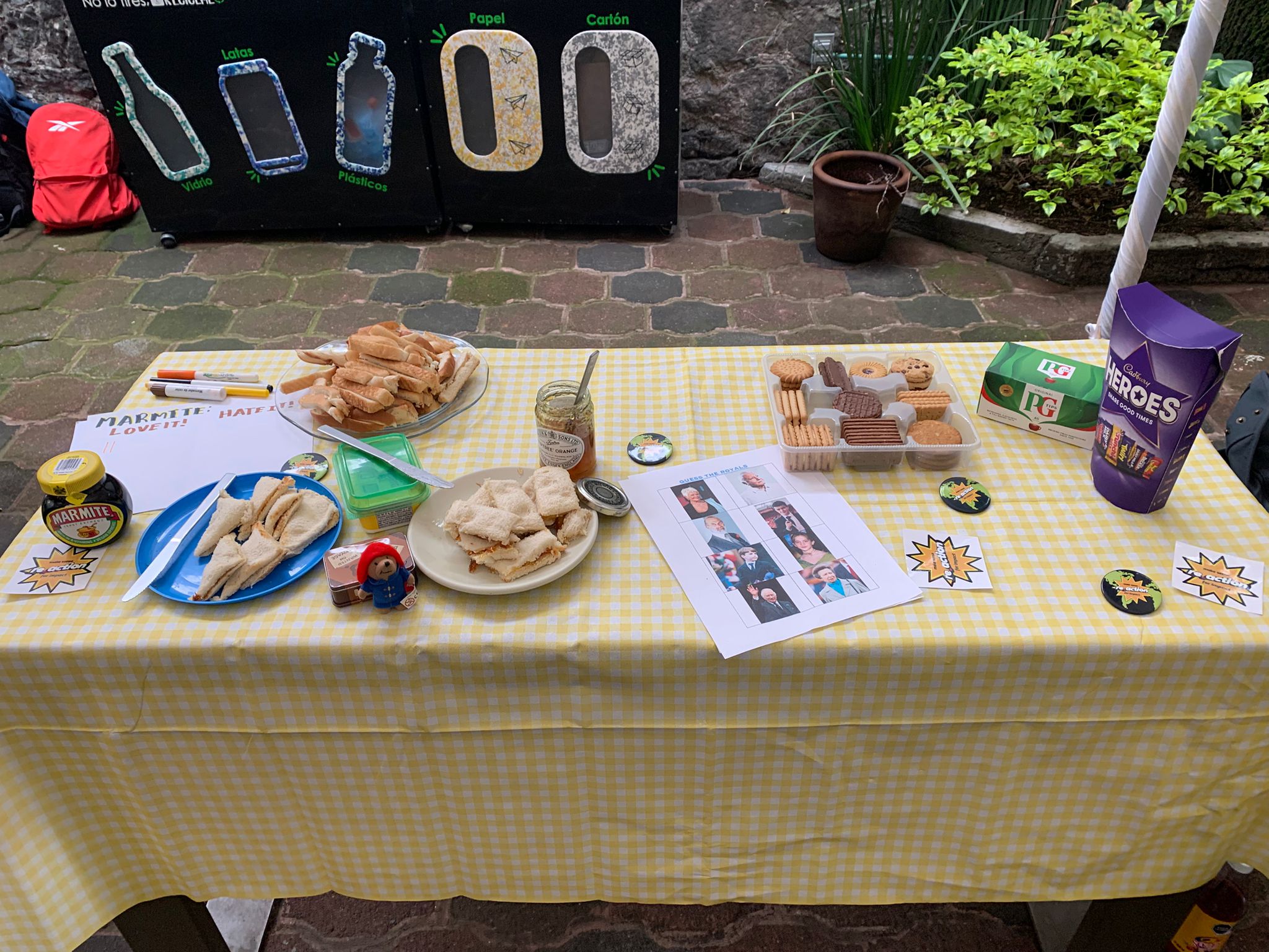 Image of a table in a yellow check cloth with marmite and marmalade sandwiches, a box of biscuits, mugs, chocolate, a guess the royals game, and a poll entitled, 'Marmite: Love it or Hate it'.
