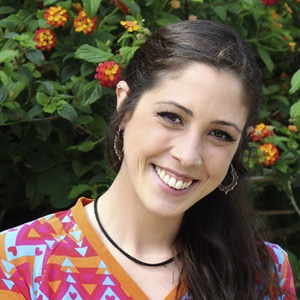 Close up portrait of Inês Mahú smiling at the camera with a tree in flower behind her.