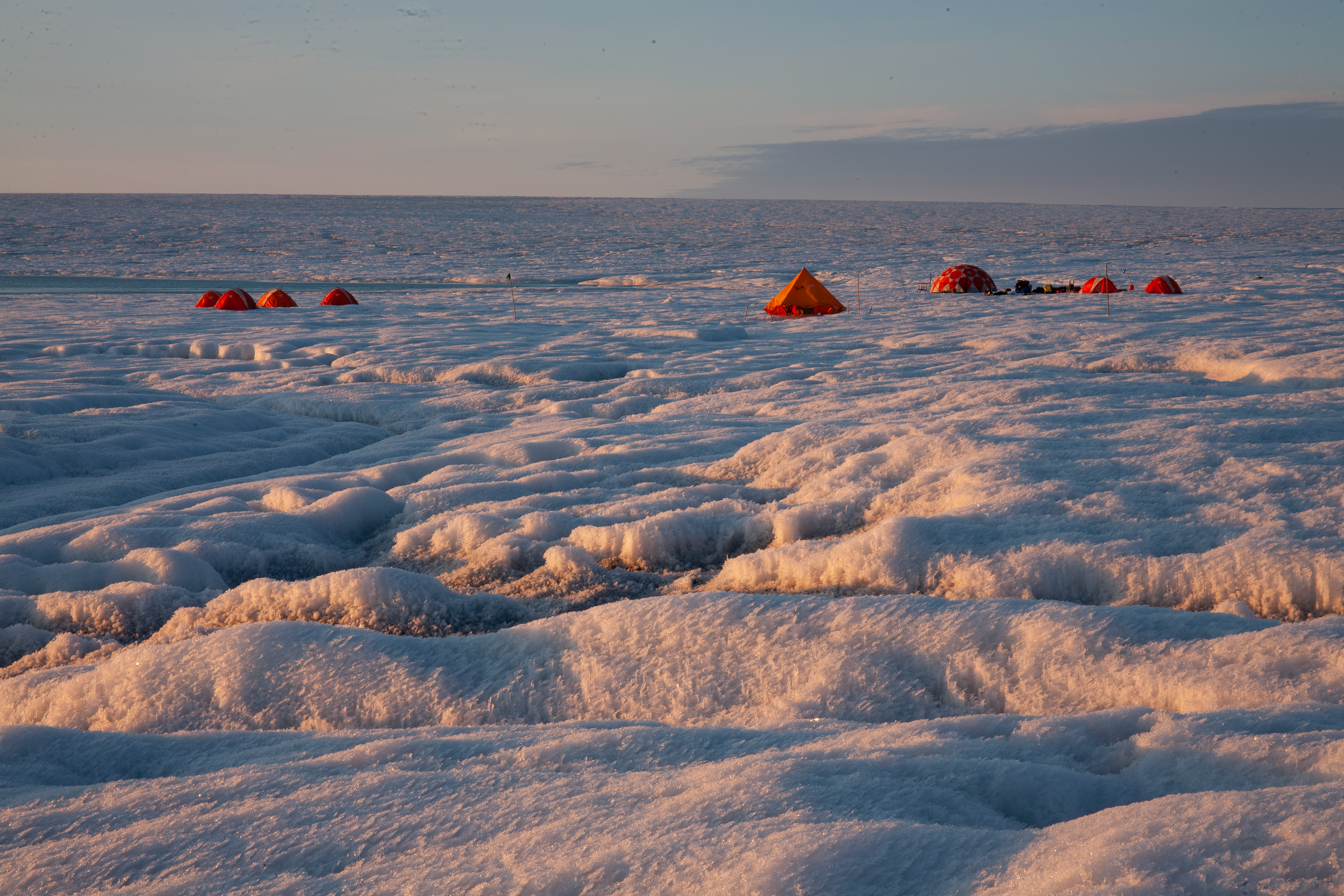 Photograph of the researcher's field camp on the ice sheet surface, with sun glint off the weathered ice in the foreground demonstrating the concept of albedo (reflectivity).