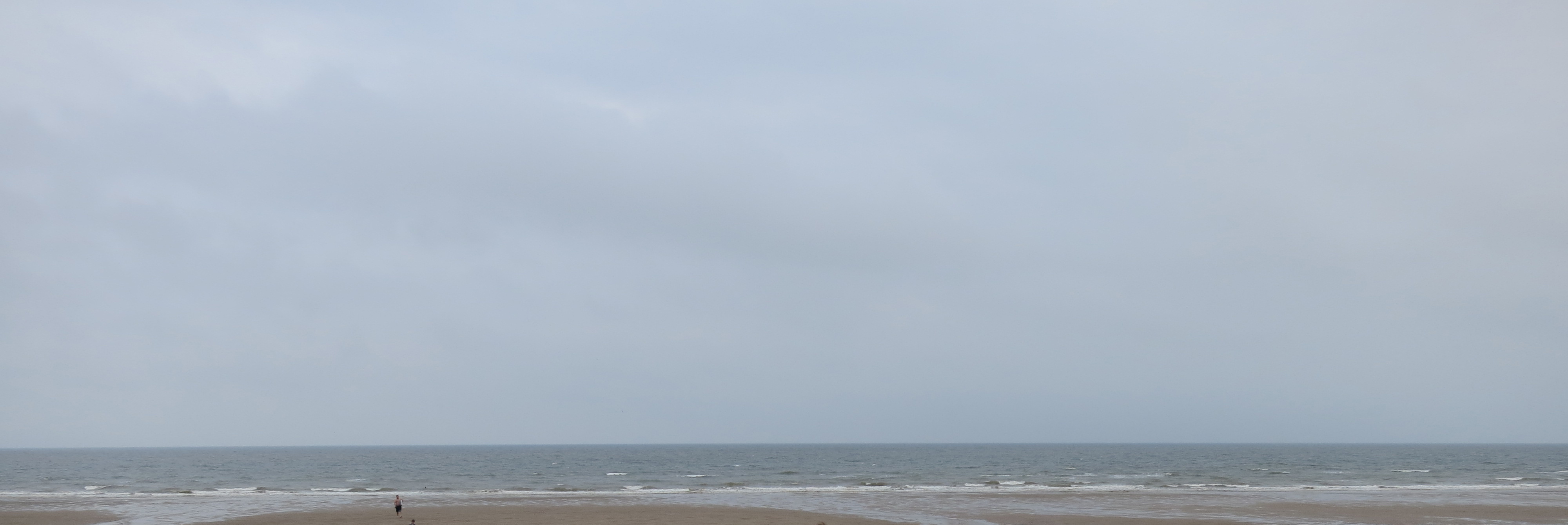 A sandy coastline under a grey sky, stretching to infinity.
