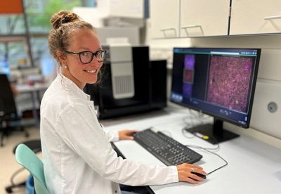 Photo of Maria Bartosova sitting at a computer in the lab doing imaging analysis, and looking at the camera smiling.