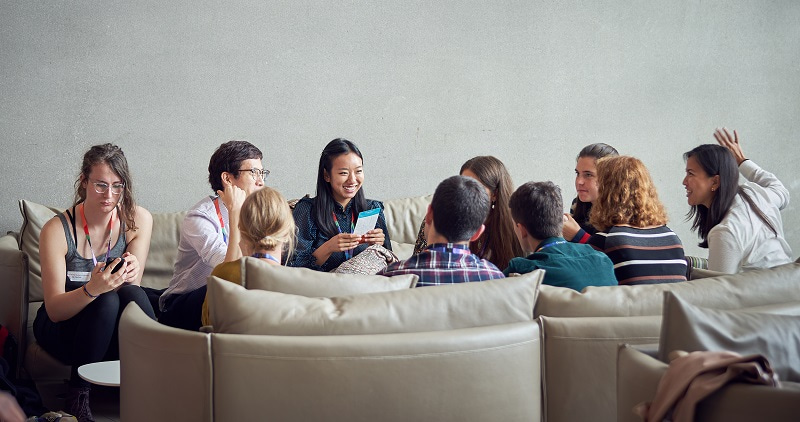 Photo taken from a distance of students sitting on sofas and taking.