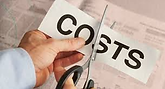 Hands holding scissors cut "COSTS" on paper against a newspaper background, suggesting cost reduction or savings.