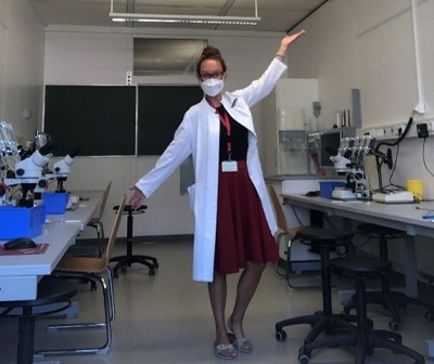 Photo of Maria standing in a teaching lab with arms outstretched.