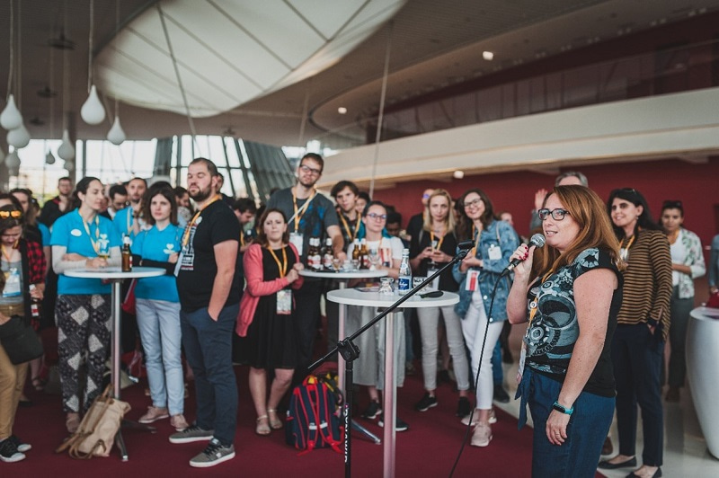 Group photo of young scientists standing around, with a young woman standing at the front holding a microphone.