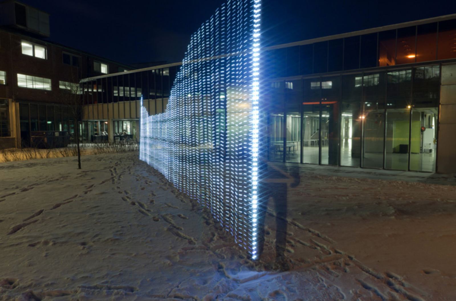 Glowing transparent light pattern overlaid on a nighttime building scene. There is snow on the ground. 