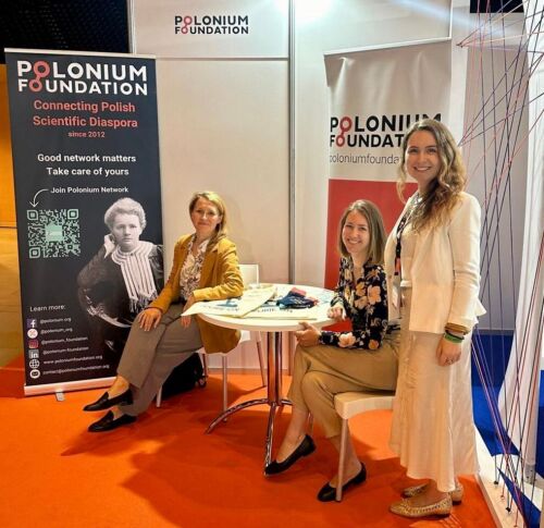 Photo showing three members of the Polonium Foundation standing or sitting around a table, with banners behind them.