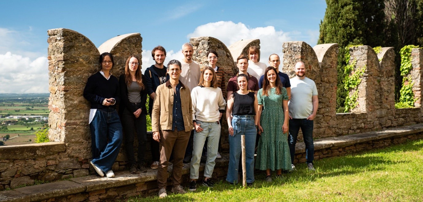 Group photo of 13 people standing in front of stone structure.