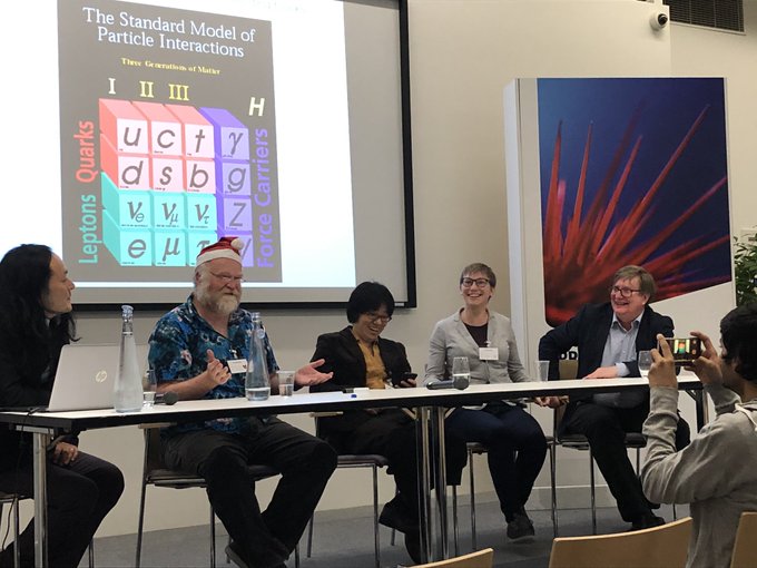 Five panelists smiling, sat behind a desk. Mark Vagins (second from left) wears a santa hat.