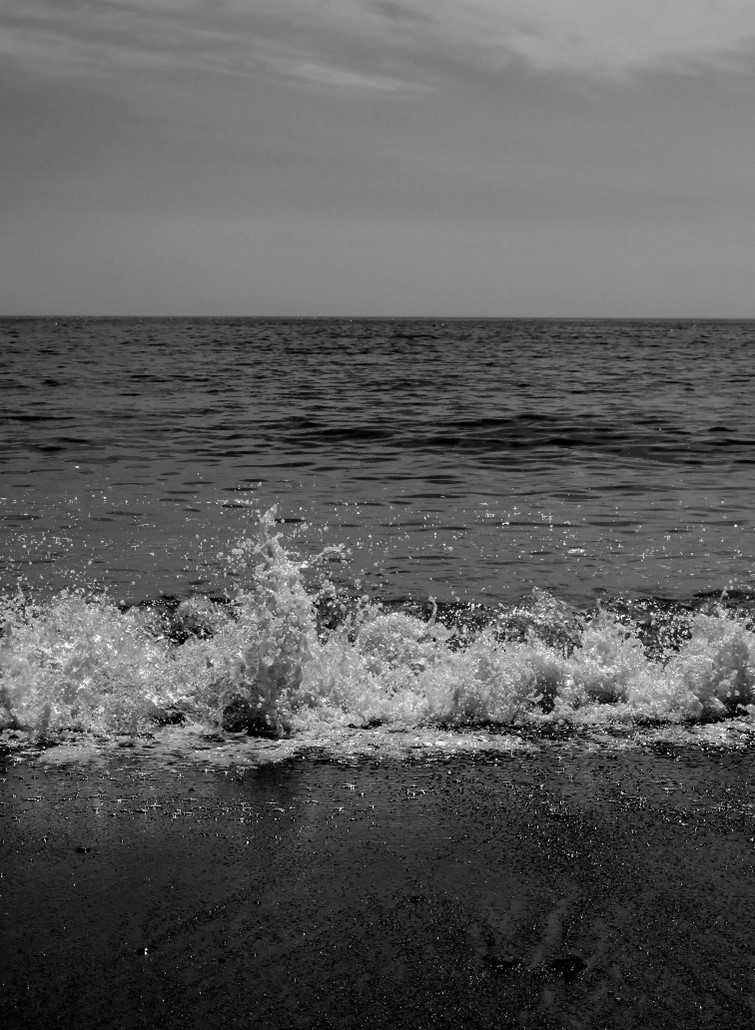 Photo of waves crashing against the beach in black and white.