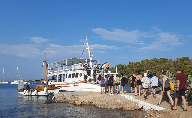 Photo from the beach of a moored boat with young people boarding it in order.