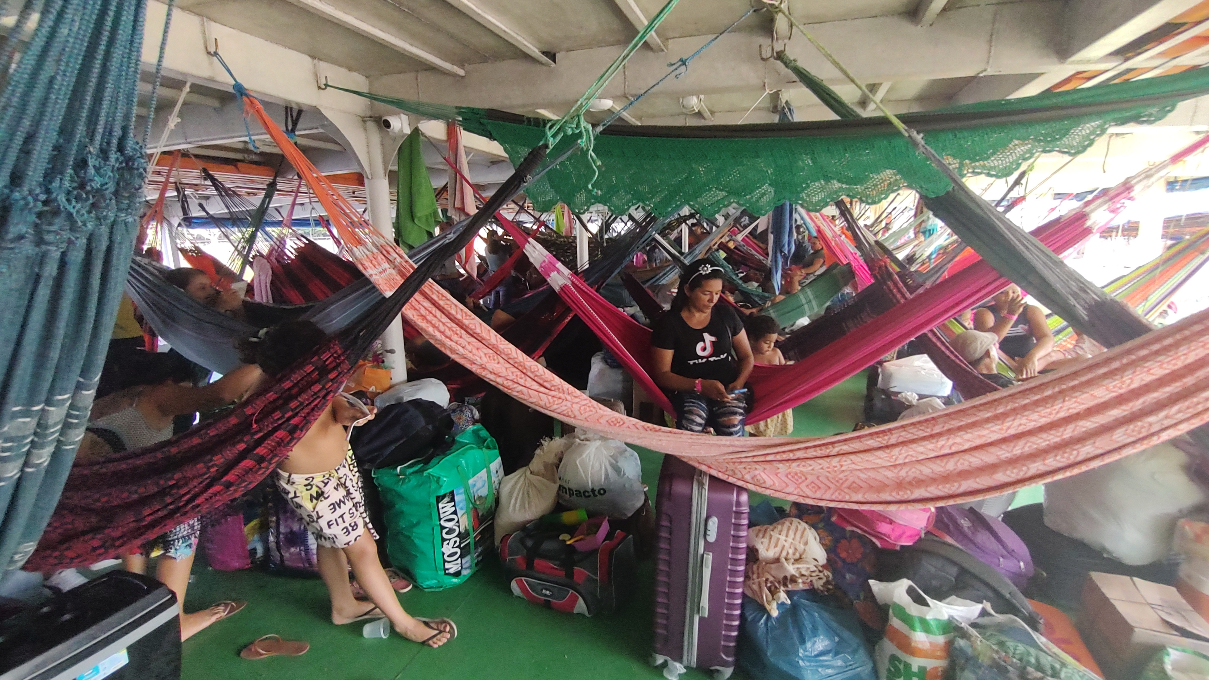 Passengers of a mid-sized boat sitting in their hammocks waiting for departure at the Port of Manaus, Brazil.