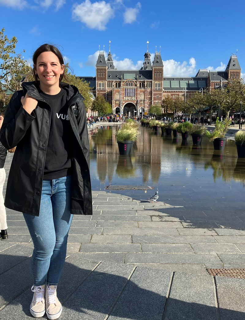Photo of Carolin Haag facing the camera and smiling in front of the Rijksmuseum, Amsterdam.