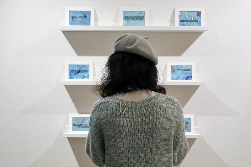 Photograph of a person from behind watching artwork displayed on the wall. Created by Molly Macleod in collaboration with Ester Bonmati, Alexander Ney, Stephen Pereira, Alexander Grimwood, a group of people affected directly and indirectly by pancreatic cancer, the Wellcome / EPSRC Centre for Interventional and Surgical Sciences at University College London and the University of the Arts, London Post Graduate Community. Creative commons licence CC BY-SA 4.0. Photograph by Catriona Mahmoud, University of the Arts, London.