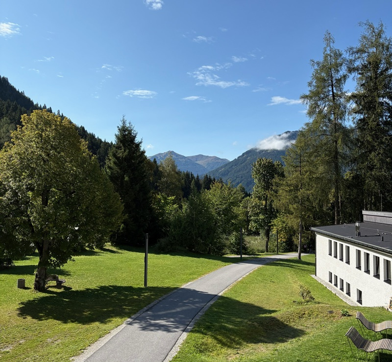 Photos of path going through trees with mountains in the background and a building on the nearby right.
