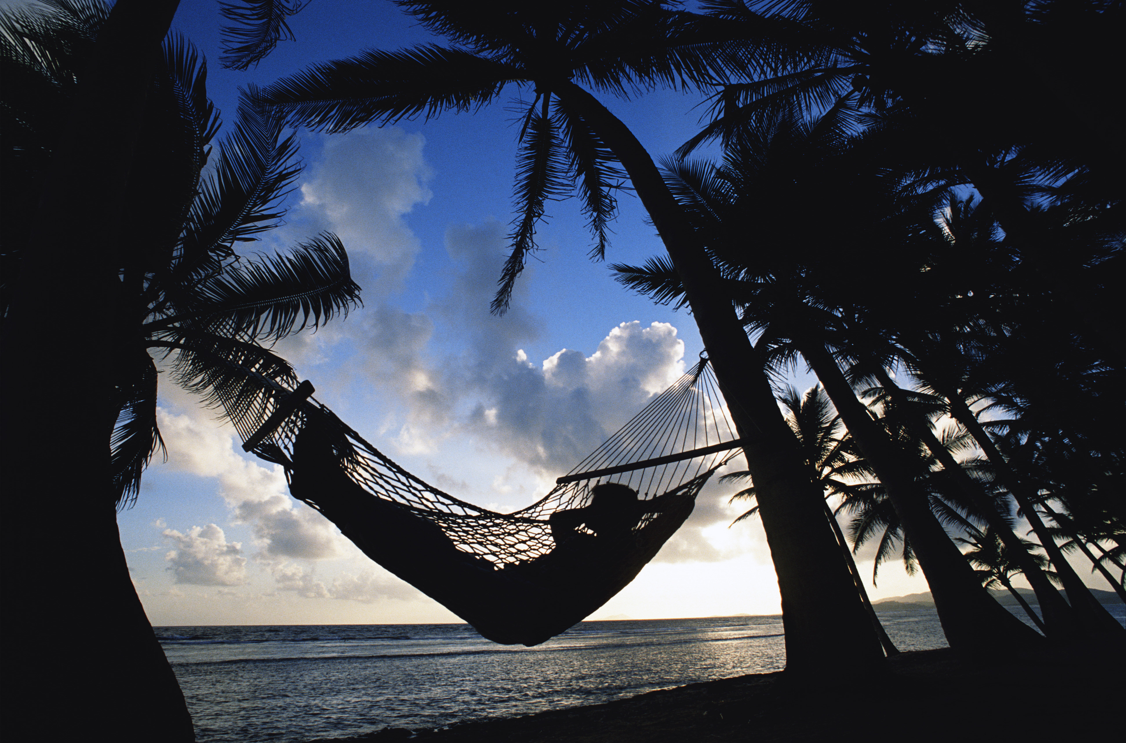 A person in a hammock at sunset, overlooking a beach