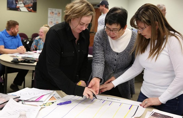 Photo showing three women discussing the content on a paper on a table in front of them, representing a workshop at HHMI BioInteractive. Image by HHMI BioInteractive.
