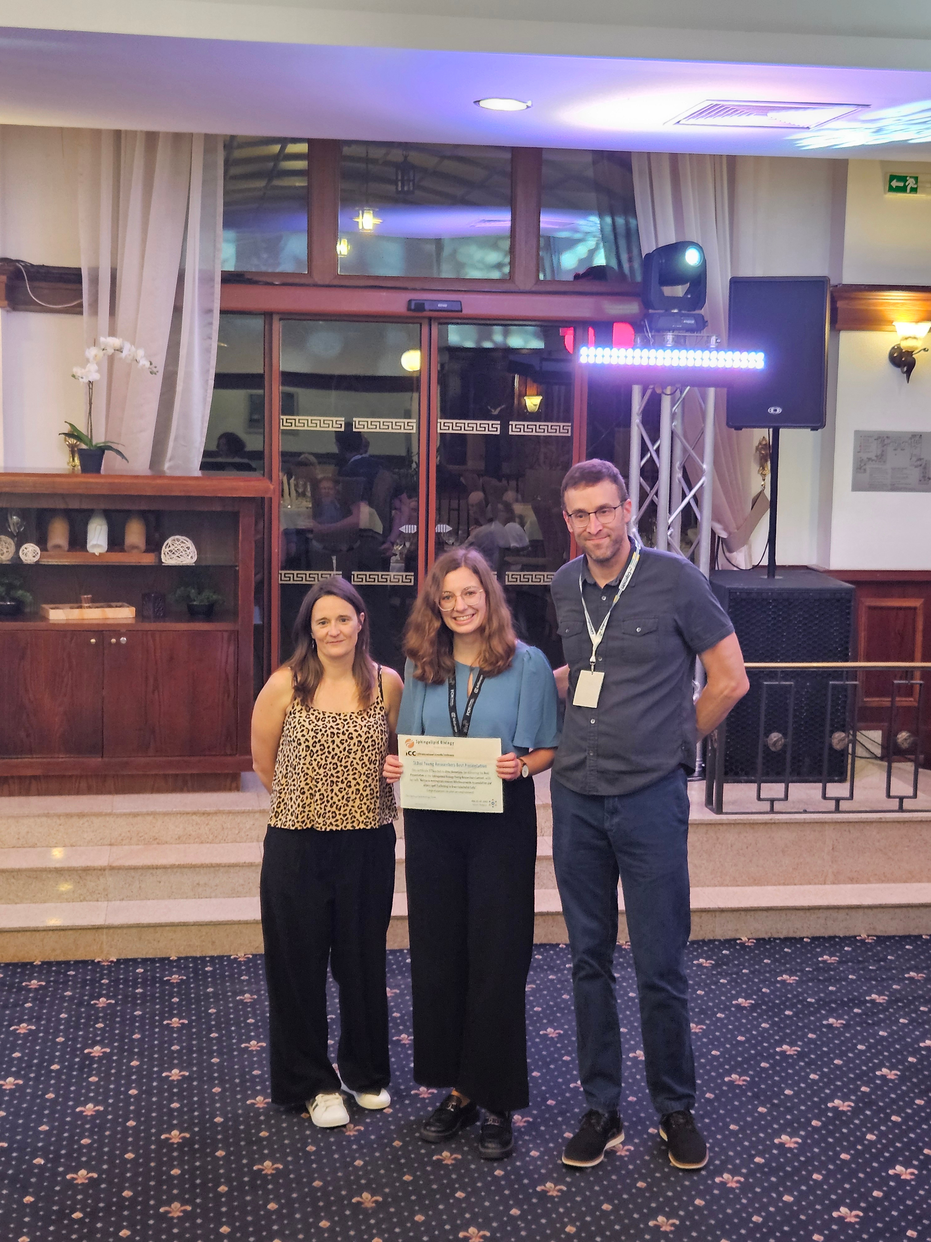 Alina holding a certificate and standing between two course organizers.
