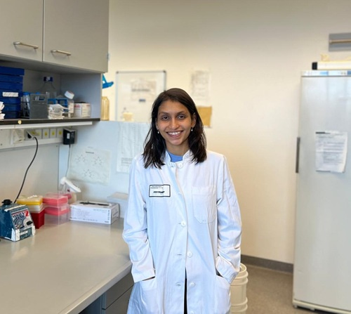 Mahima Bhat wearing a lab coat and smiling at the camera.