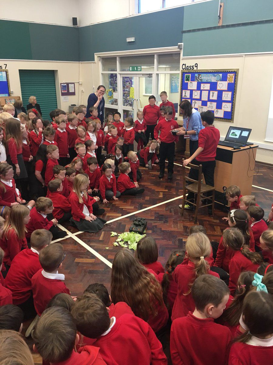 School children watching a model tank being riven over some lettuce leaves
