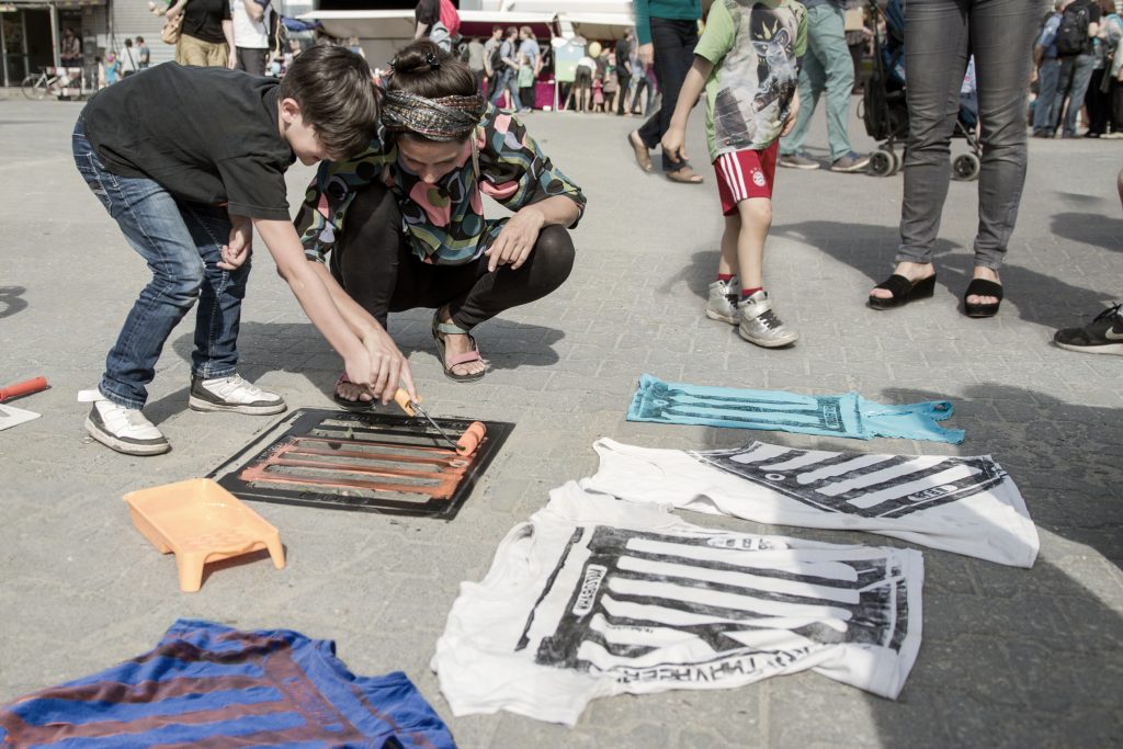 Families rolling paint and printing shirts at a community event.