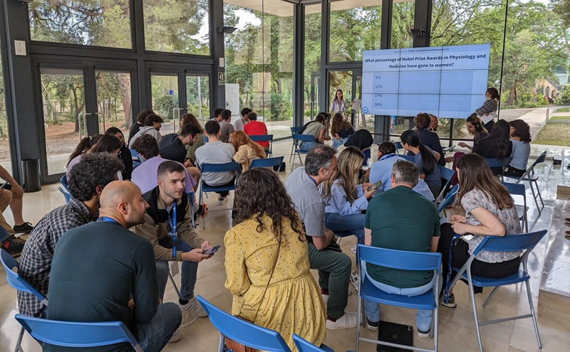 Photo of a large group of people sitting in a room and interacting.