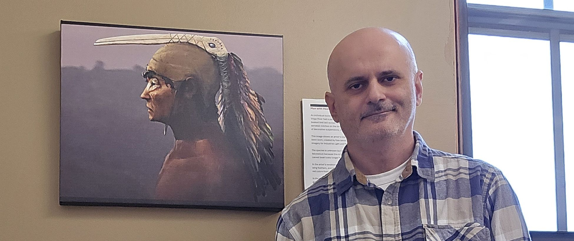 Co-author Iosif Lazaridis in front of an art print of the rendition by Russel Story22 of an Eneolithic young male from Ekaterinovka Mys grave 45 at the Department of Human Evolutionary Biology, Harvard University.