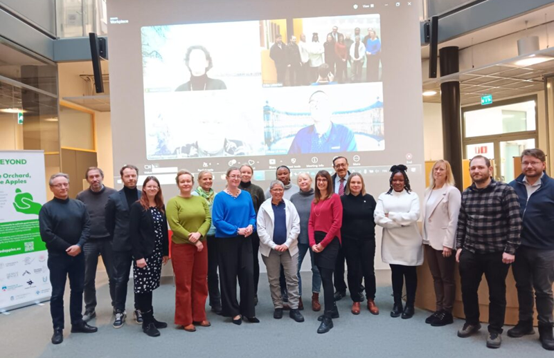 Group photo of people standing in front of a projection with other people connected online.