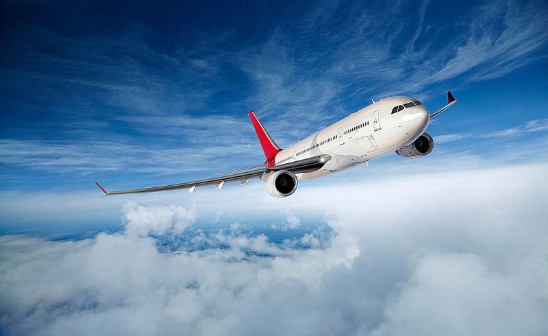 A plane flying above the clouds, shown against a blue sky with some clouds.