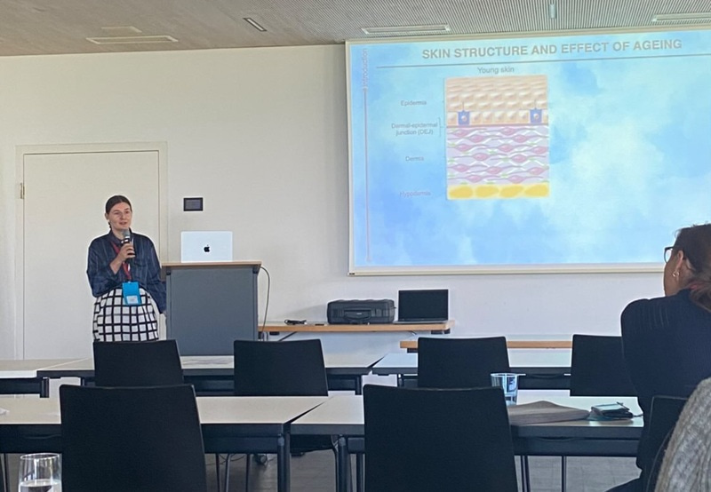 Photo of young woman holding a microphone and standing next to a podium and projected slides.